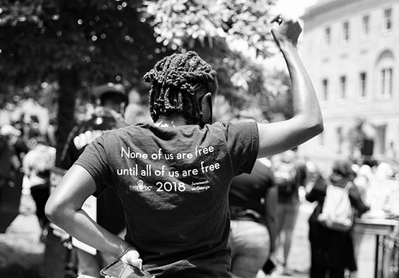 Image showing the back of a young african american woman's t-shirt that reads none of us are free until all of us are free